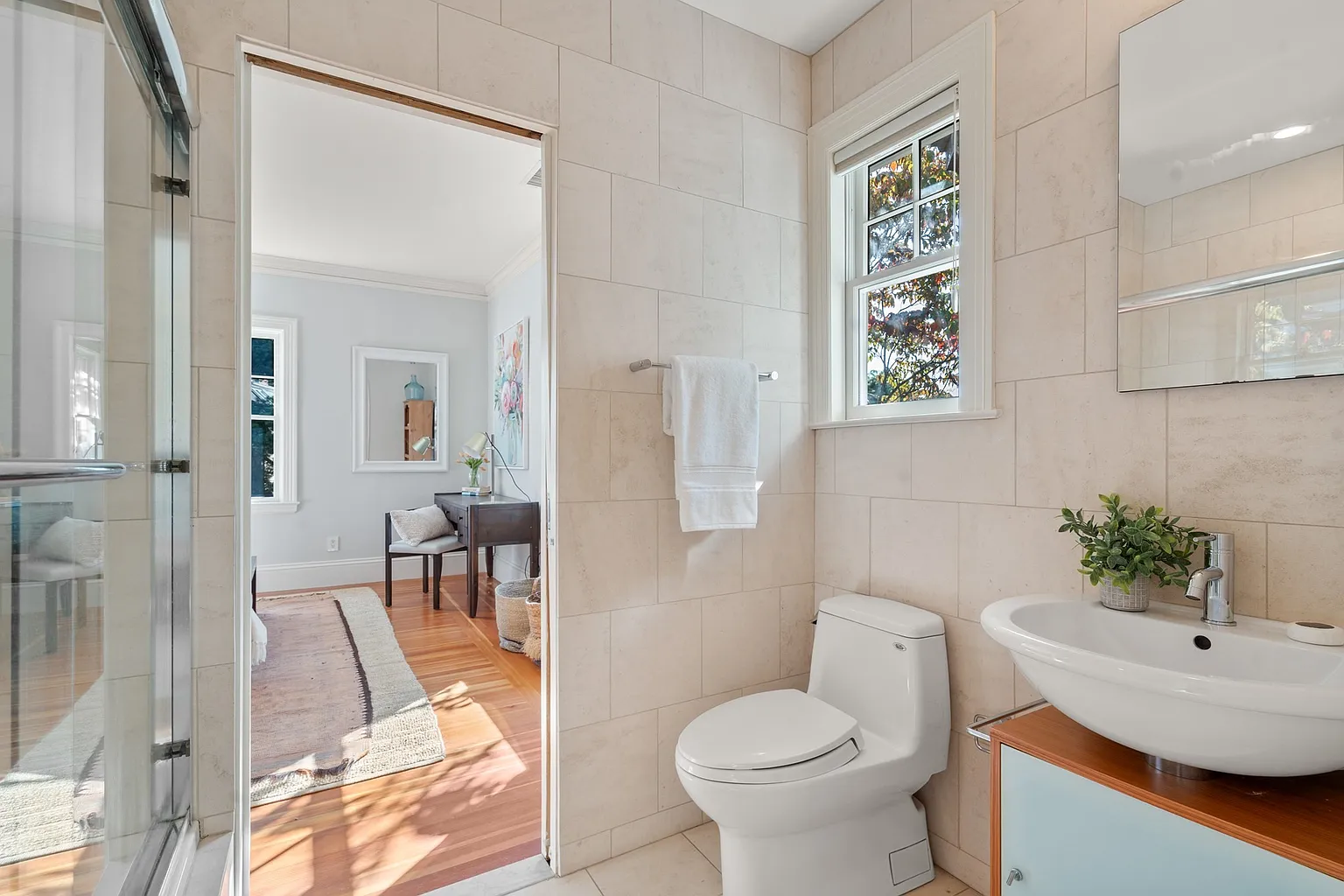 This suite's bathroom is finished in pale stone tile, with a glass-enclosed shower sitting across from a compact single vanity.