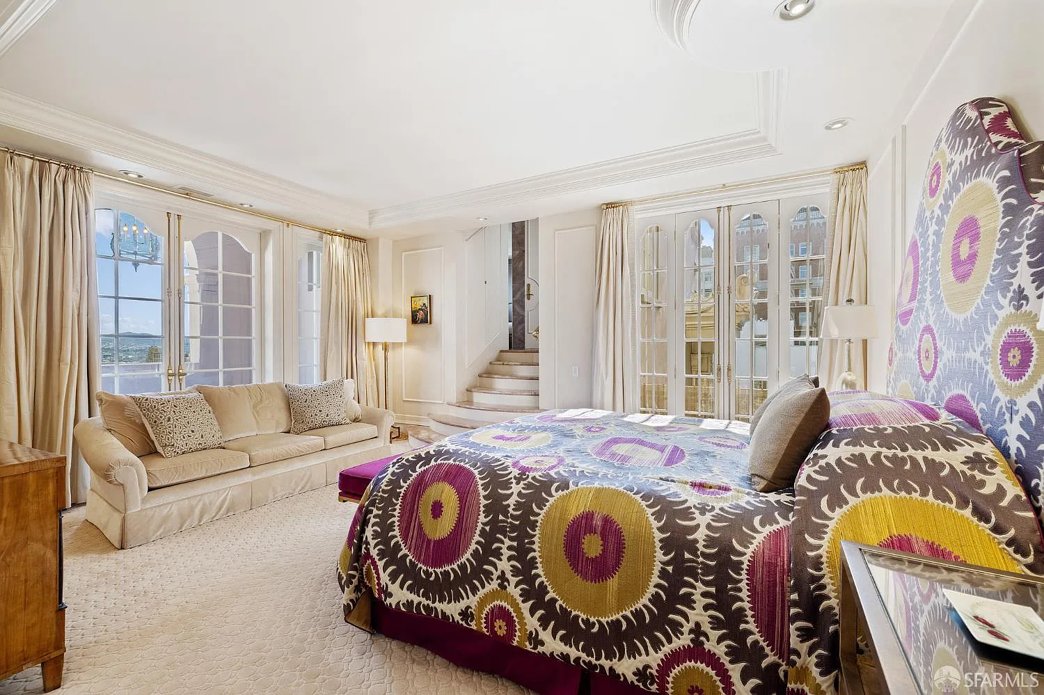 A patterned bed sits at the center facing a sofa, and a short set of steps rises toward the connected bath.
