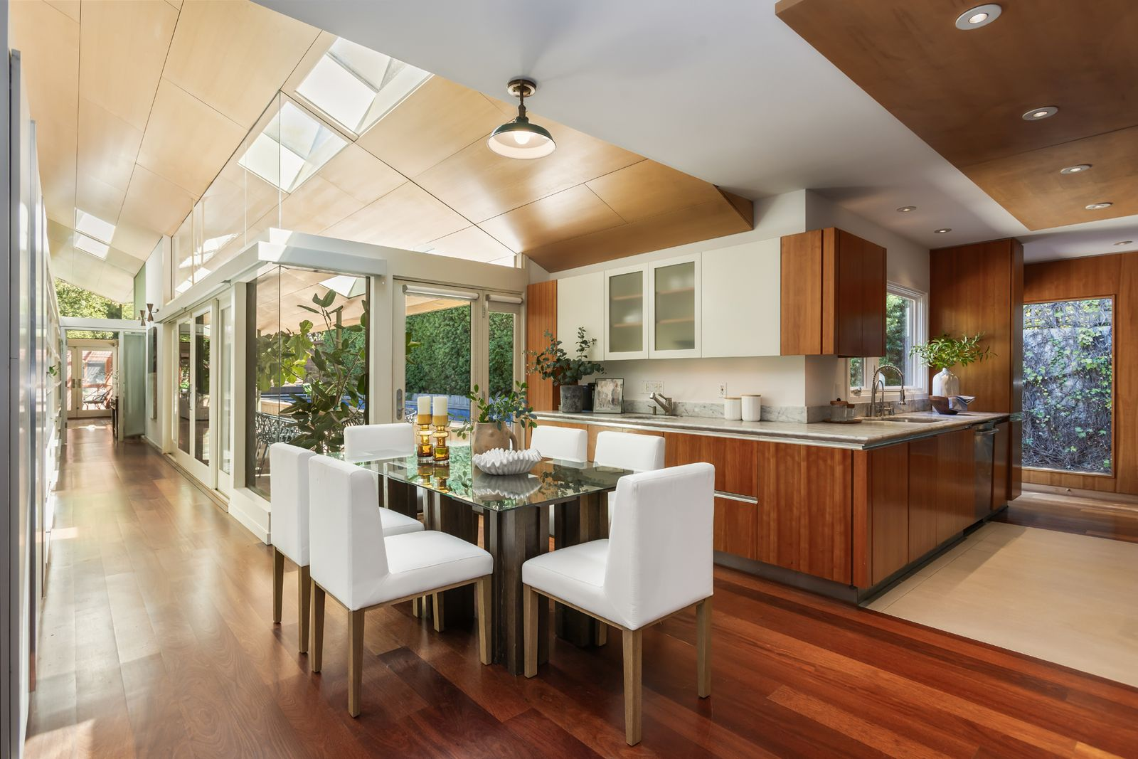 The kitchen opens into a second dining area set beneath a wood-paneled ceiling with skylights before opening to the pool terrace.