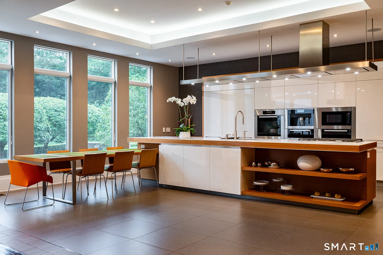 The contemporary kitchen opens around a long central island with a white countertop and warm wood detailing along the outer edge. 