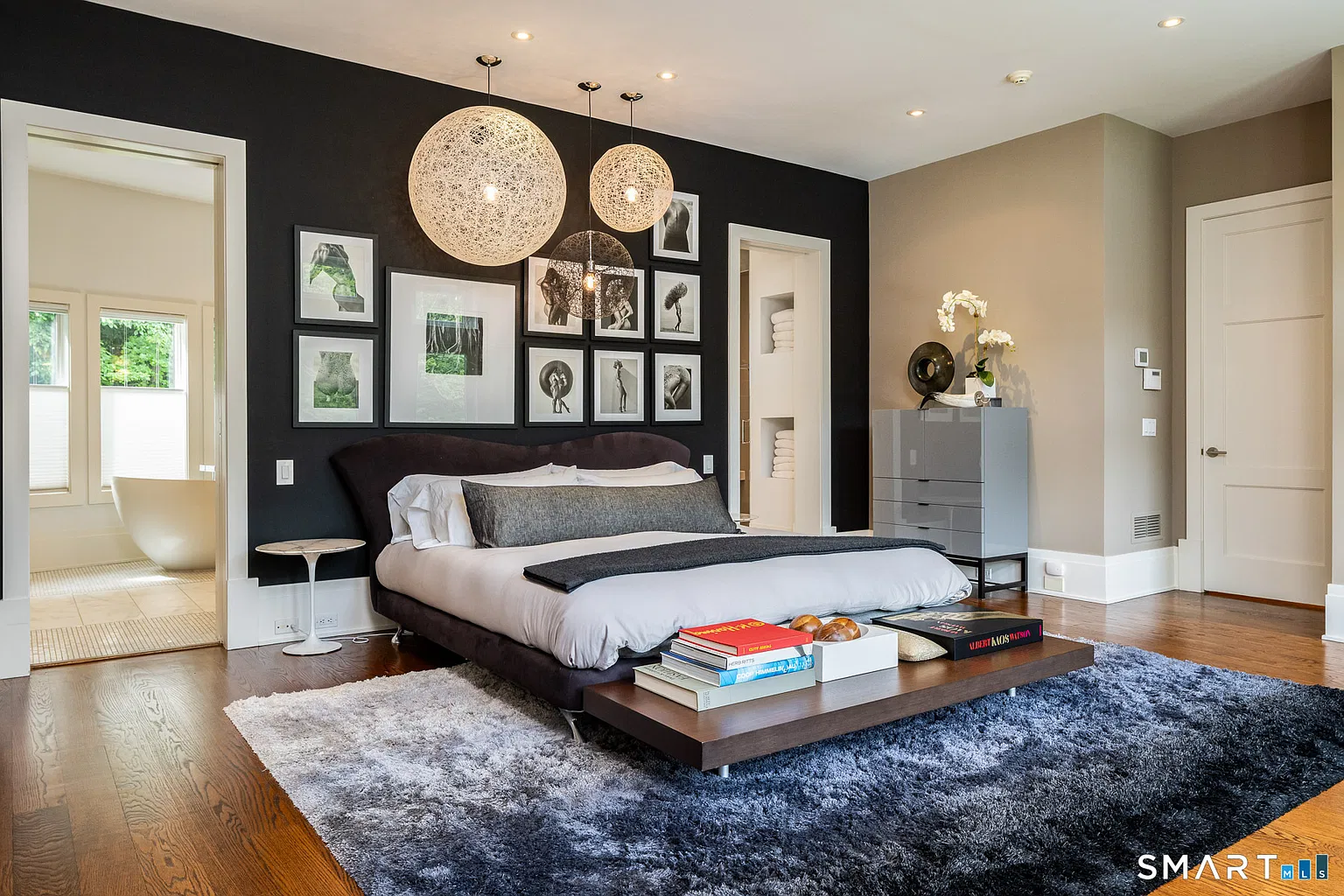  The bed sits atop a blue ombre rug, while a deep charcoal accent wall and a series of round pendant lights give the room a more dramatic flair.