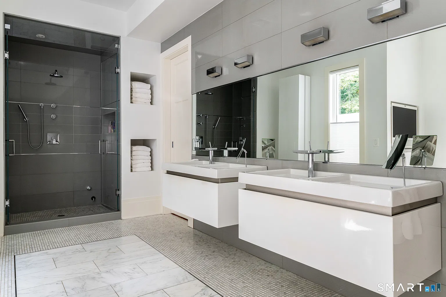 Two separate floating vanities run beneath an oversized horizontal mirror line near a glass-enclosed shower.