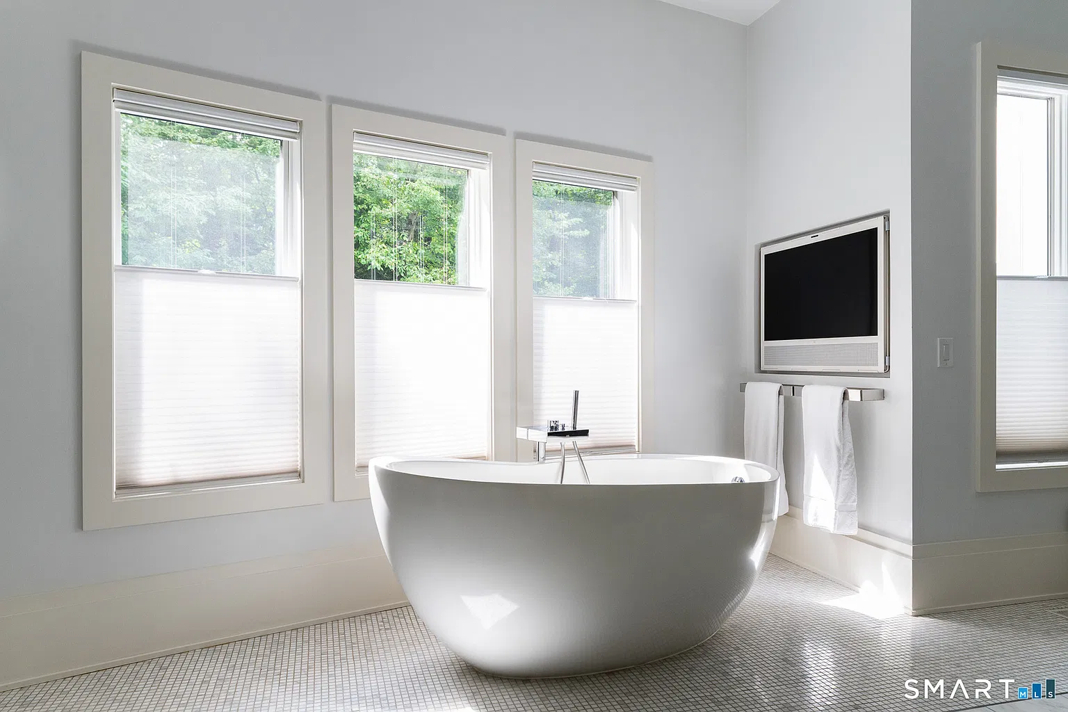 A freestanding soaking tub sits beneath a row of windows, creating a separate bathing zone away from the vanity and shower.
