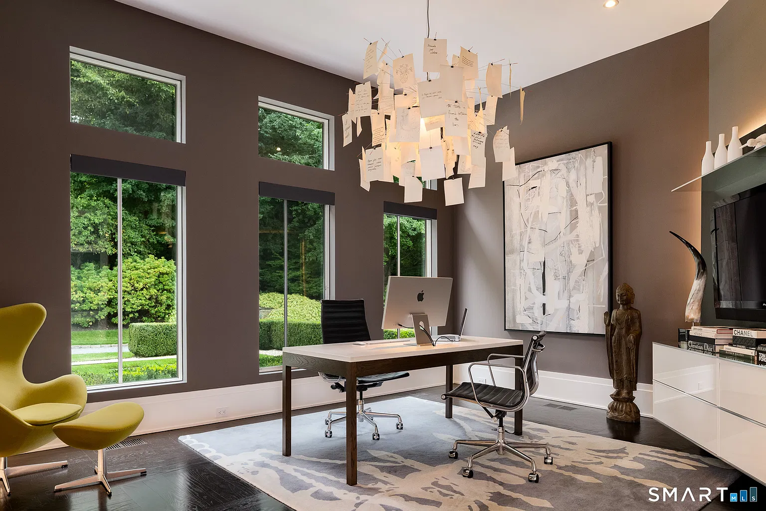 A streamlined desk sits across from a media wall, while the room’s deeper wall color and large-scale artwork give it a more formal design.