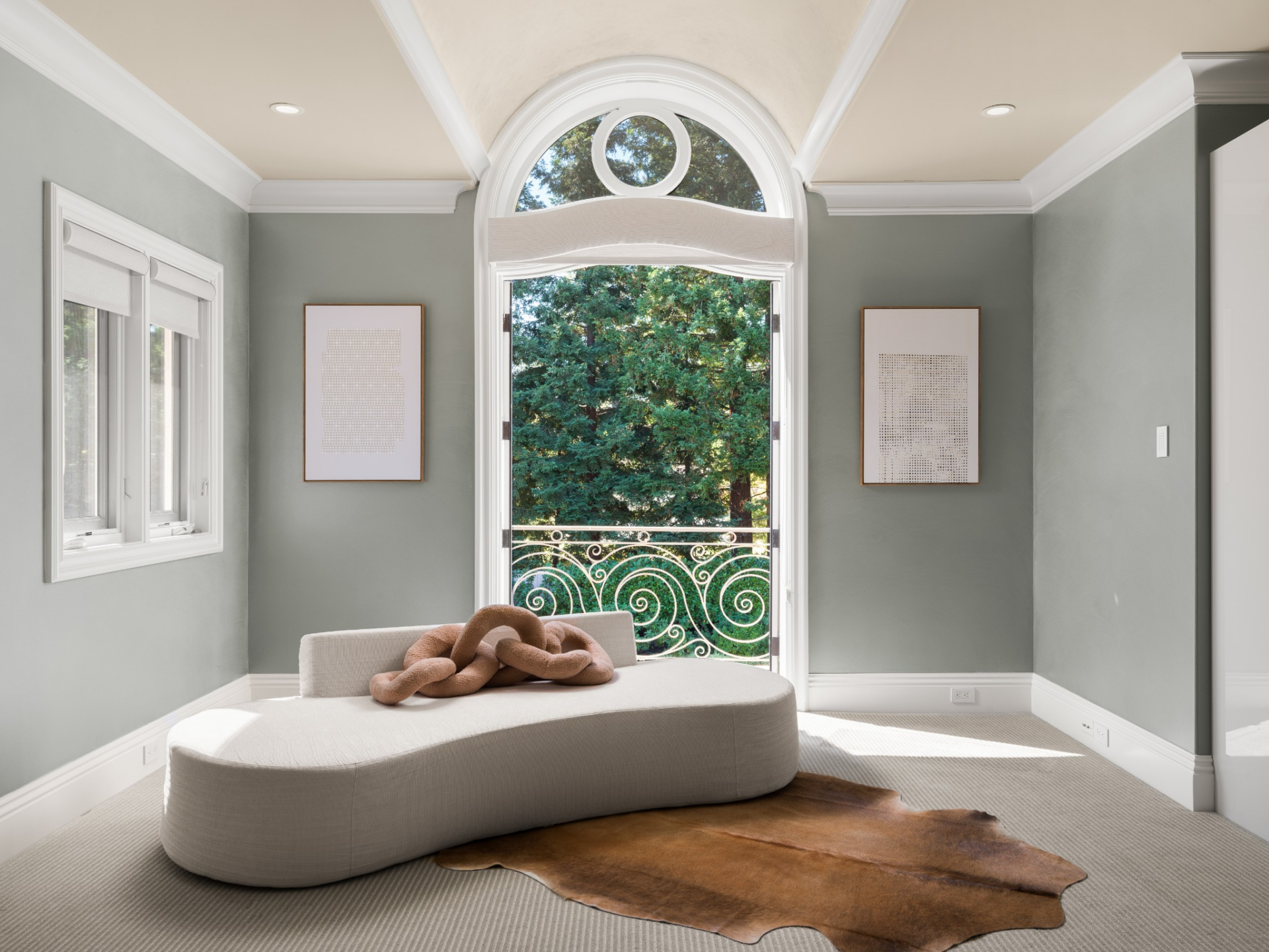 The lounge space is set against an arched glass door opening to a Juliet balcony with a view of the lawn.