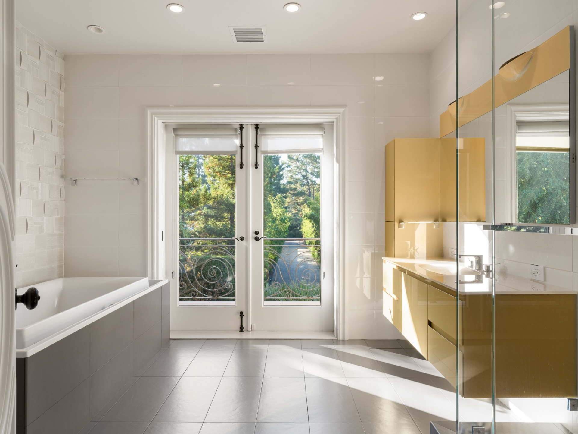 Before reaching the doors, a long floating vanity runs along one wall next to a glass-enclosed shower, while the soaking tub is placed along the other side.