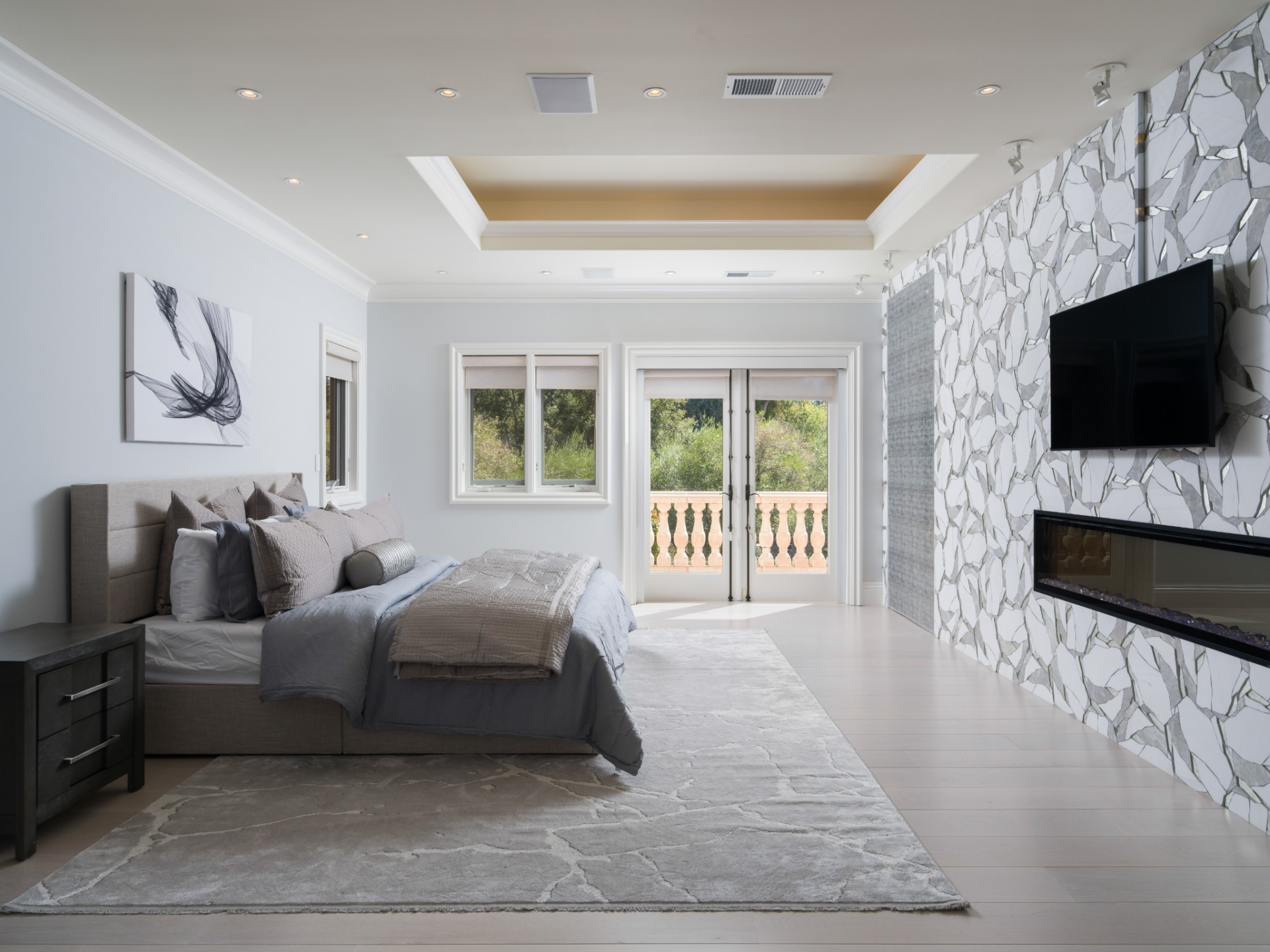 Within the bedroom, a tray ceiling runs overhead, while French doors at the far end open to a balcony.