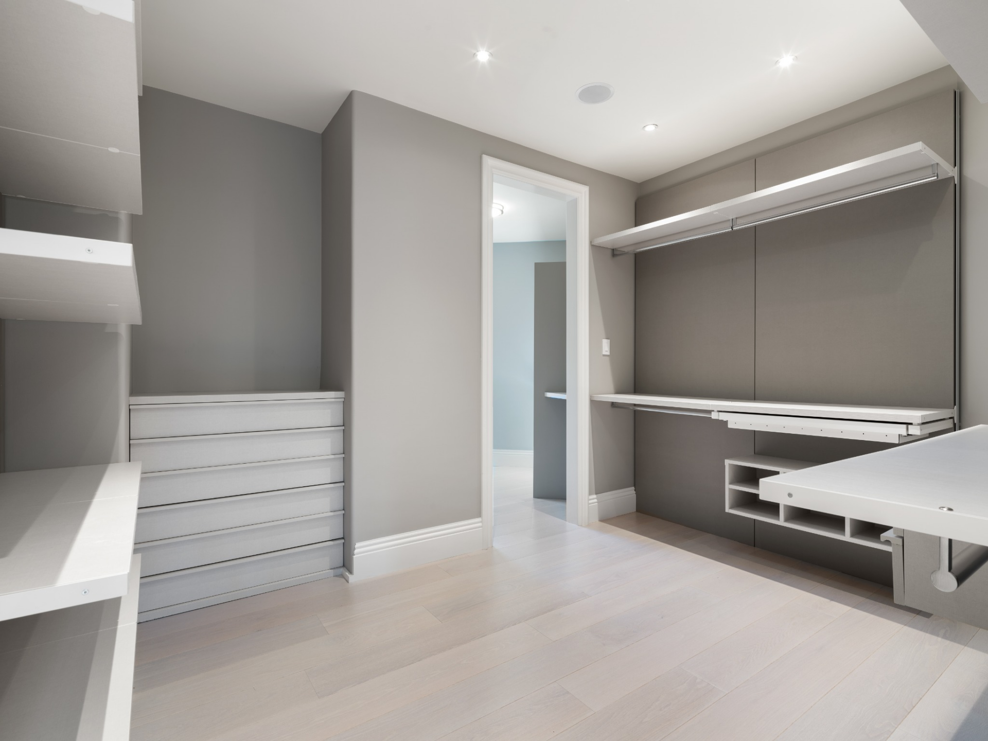 Closet with a streamlined gray palette with open hanging sections, shelving, and built-in drawers.