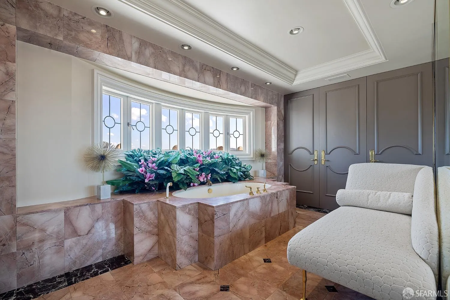A separate bathing room, where lighter stone surrounds a built-in tub set beneath a curved window bay.