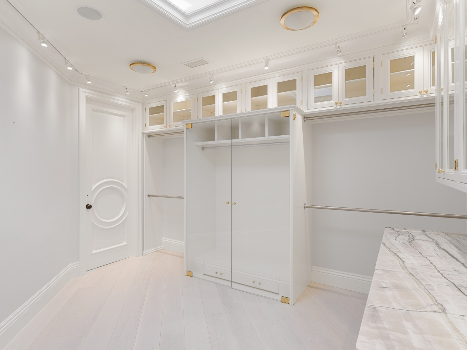 Closet with white cabinetry and marble countertops beneath glass-front upper storage.