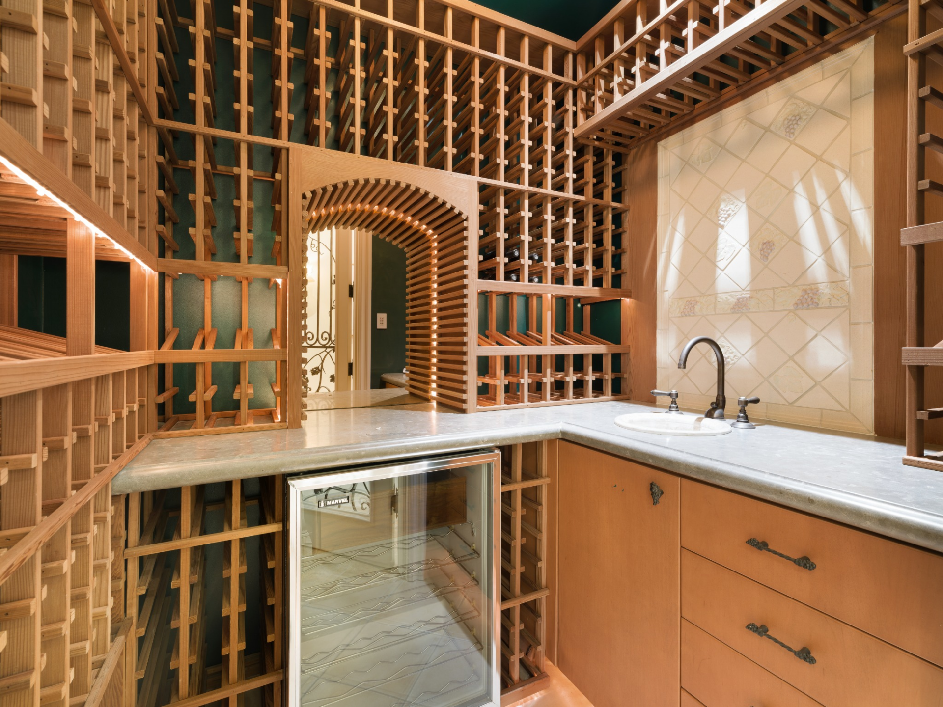 Wood racking wraps the walls and rises nearly to the ceiling, with a small counter and sink built above an undercounter wine refrigerator.