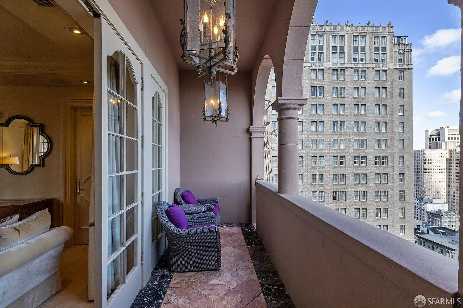 French doors open onto one of the suite’s private balconies, where a narrow covered terrace with arched openings overlooks the surrounding city.