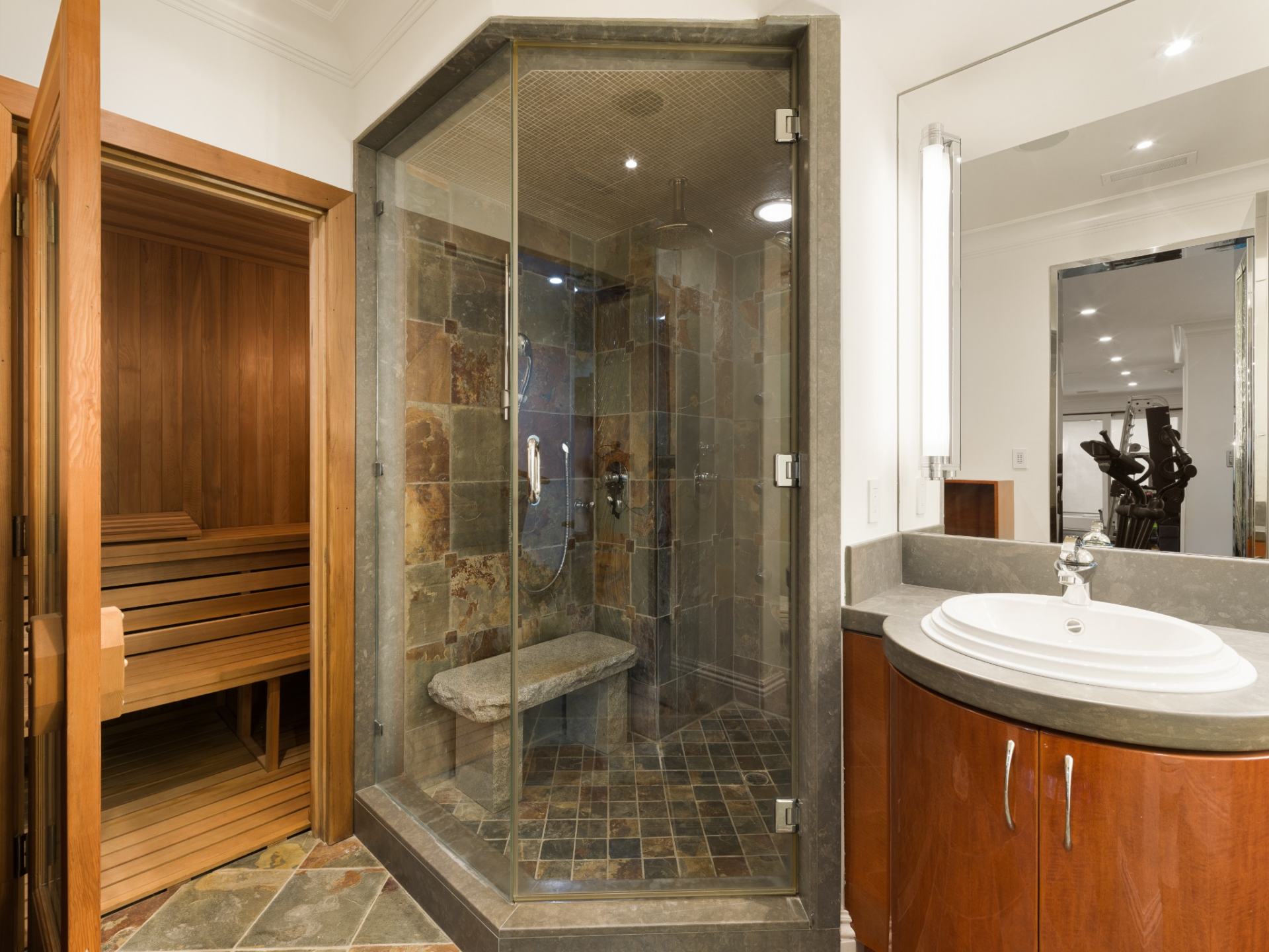 A separate recovery area consisting of a glass-enclosed steam shower, a wood-lined sauna, and a vanity.