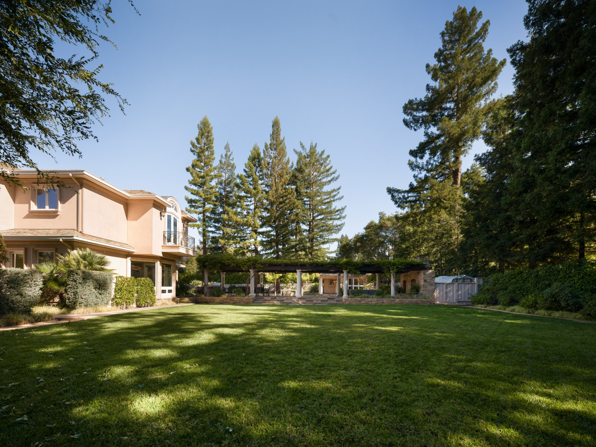 Directly behind the house, a vine-covered veranda runs parallel to the main lawn, shaded by the tree's branches.