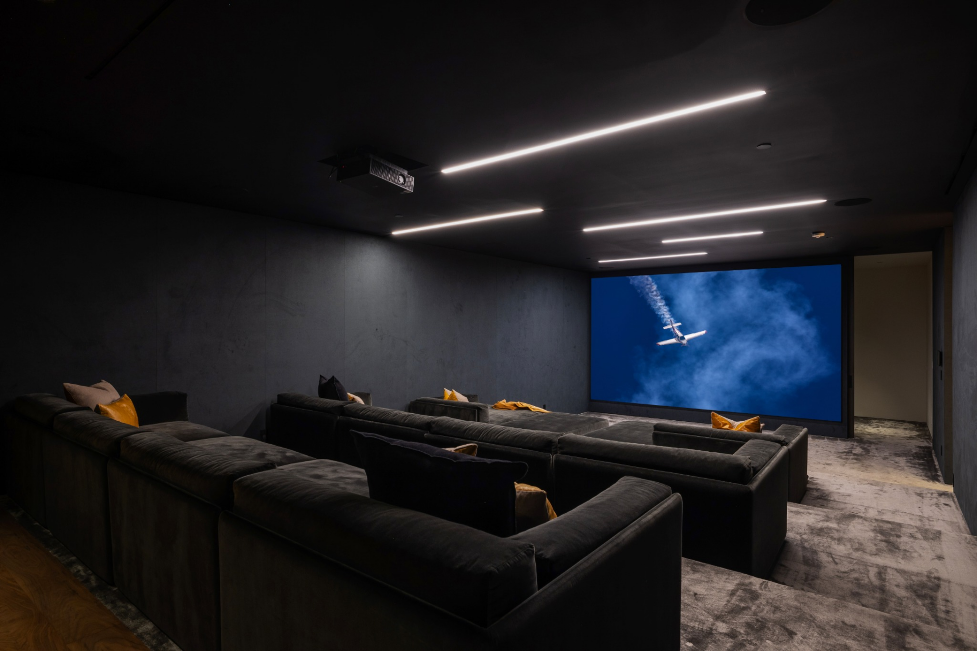 The theater has several rows of oversized lounge seating facing toward a full-width projection screen. 