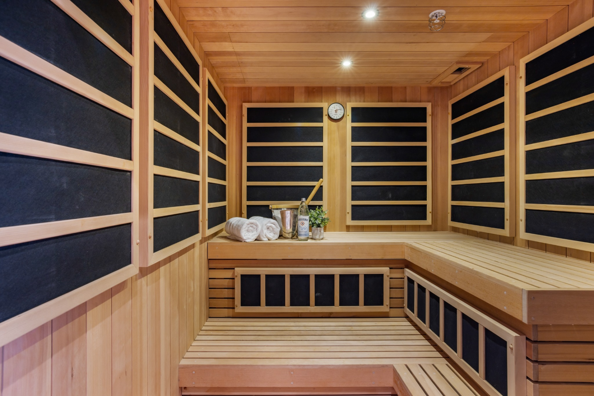 The sauna is lined almost entirely in warm wood, with tiered benches wrapping the perimeter beneath a series of dark infrared panels.
