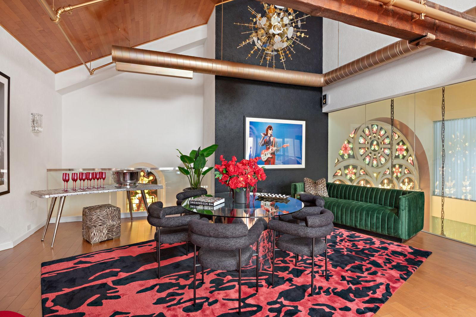 The space opens around a central round table with chairs, while a green velvet sofa is pushed toward the glass wall.