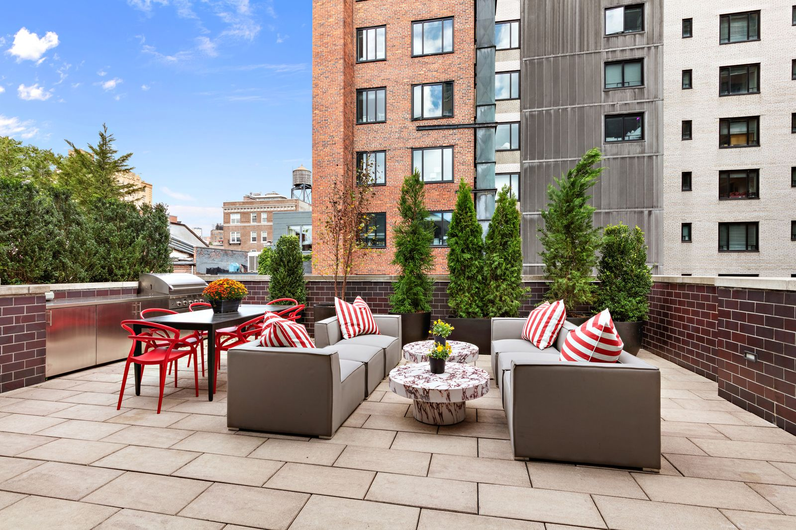 Stone paving extends across the full terrace, where a dining area and separate outdoor lounge sit alongside the outdoor kitchen.