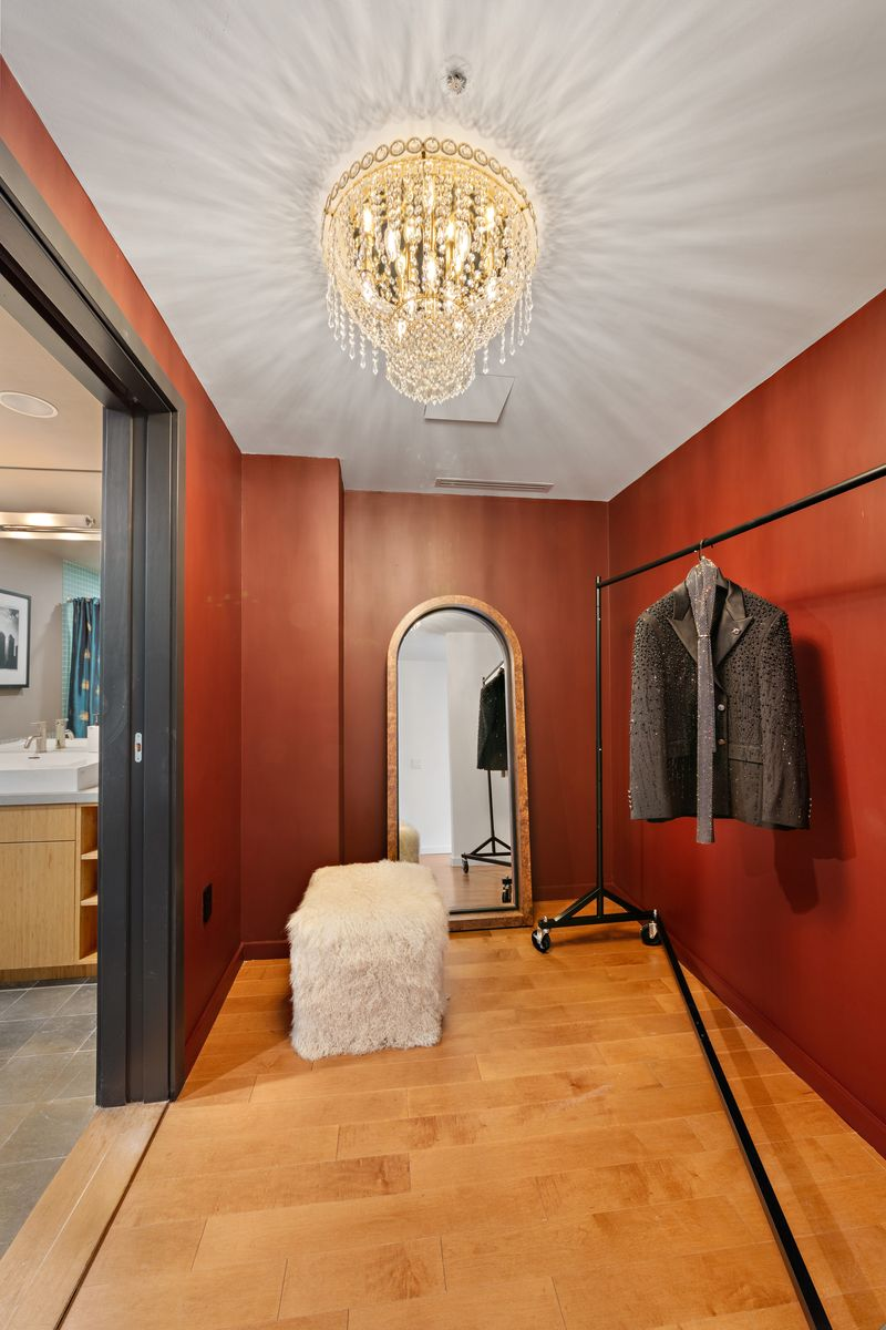 The red painted walls continue into a walk-in closet, with hanging space running along one wall beneath a crystal chandelier and a full-length mirror placed at the far end.