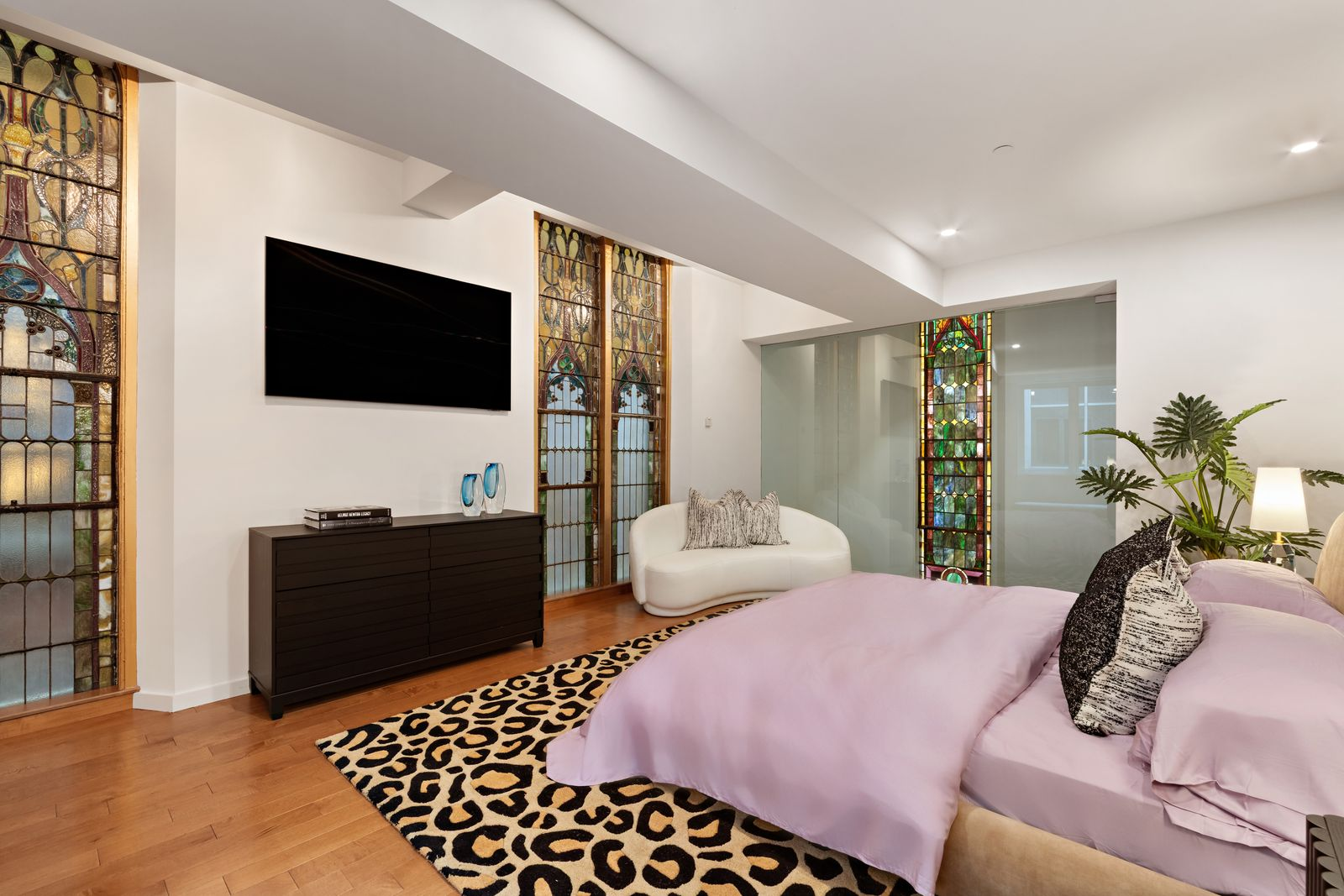 The bedroom is framed by sections of the building’s original stained glass, with the bed set across from the windows.