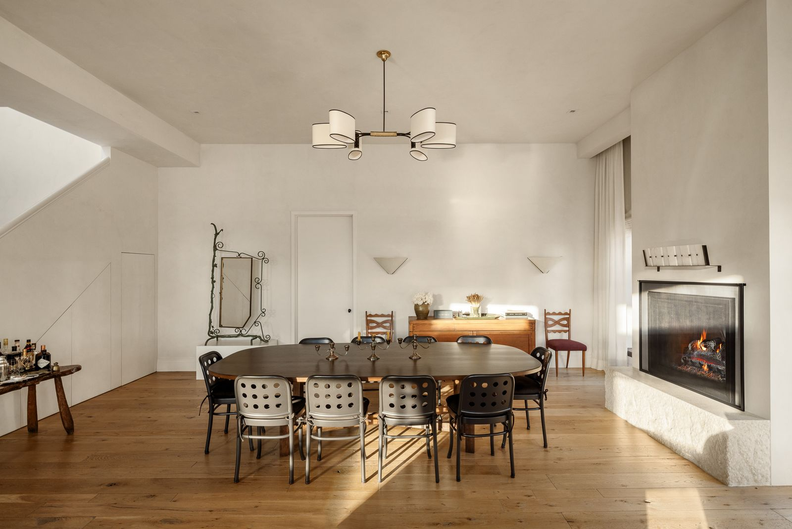 In the corner of the room, the dining area sits beneath a modern chandelier and next to a travertine fireplace.
