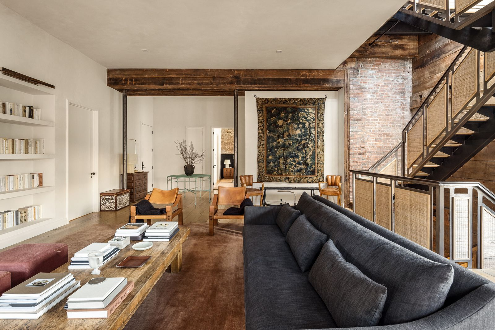 At the back of the room, a split staircase is surrounded by walls of exposed brick and wood planks, with one side descending to the lower level and the other continuing upward toward the rooftop terrace.