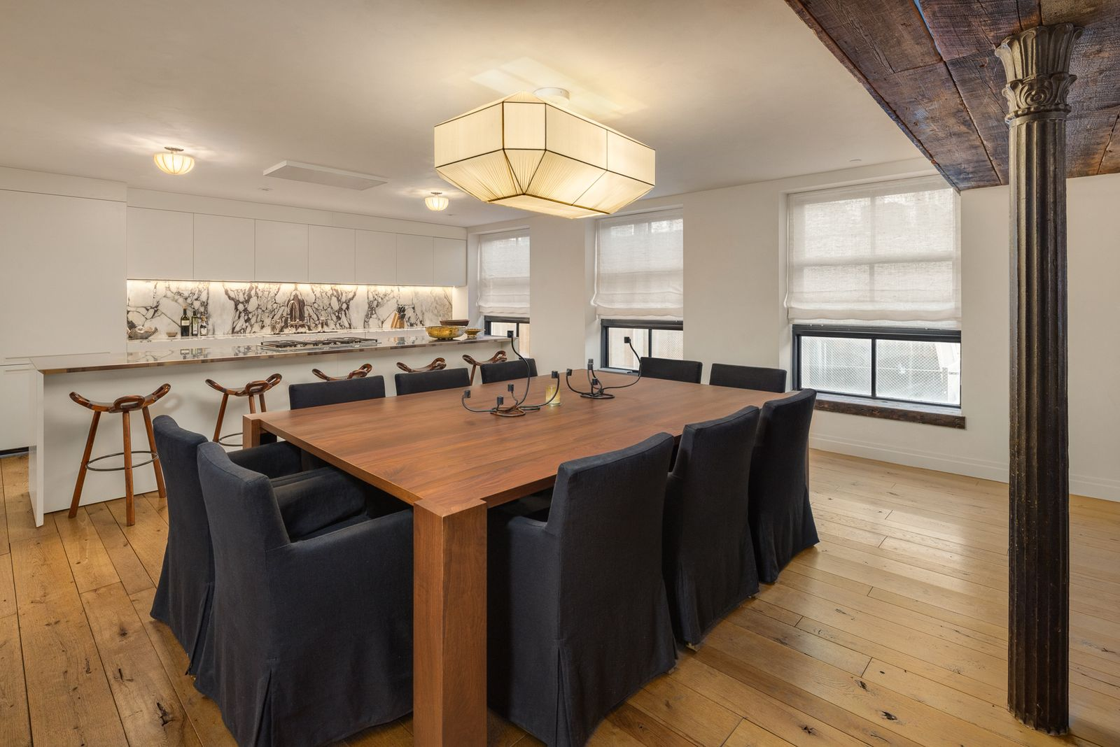 White cabinetry and stone surfaces wrap the cooking space, while a large dining table for ten sits on the other side of a long island lined with barstools.