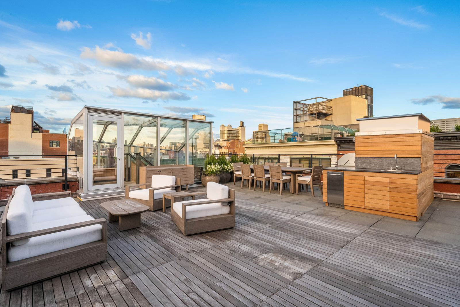 Wood decking and stone paving divide the roof into lounging, dining, and cooking areas, with a full outdoor kitchen positioned beside the long dining table.