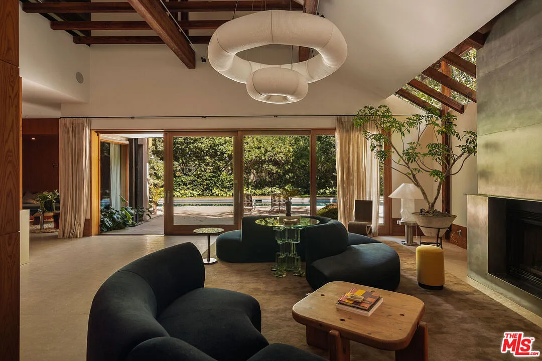 Curved sofas and low tables fill the center, while a series of glass doors across the opposite wall opens directly to the pool terrace and surrounding gardens.