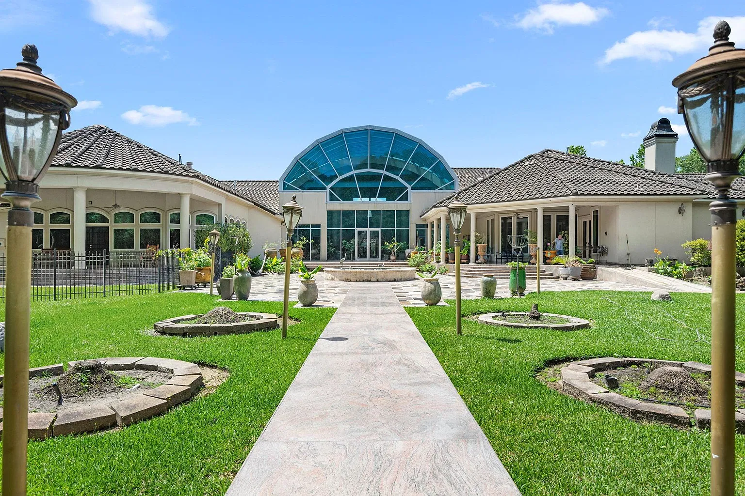 The glass-enclosed atrium and the living spaces around it open directly to a central courtyard, where paved walkways extend through sections of lawn framed by trees and landscaping.