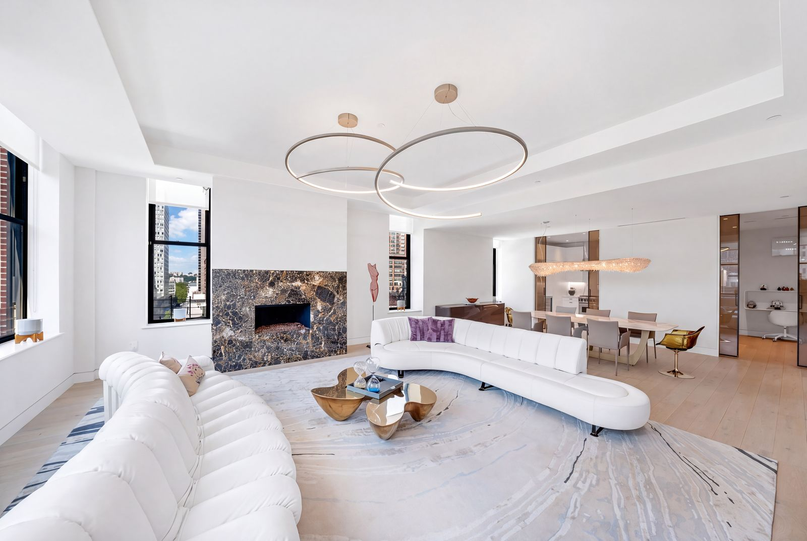The main living area is gathered around a contemporary dark stone fireplace, with two curved white sofas facing each other beneath a pair of sculptural ring chandeliers.