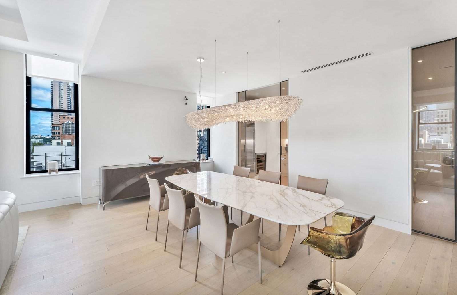 The great room moves into a formal dining space with a long marble-topped table beneath an elongated crystal chandelier.