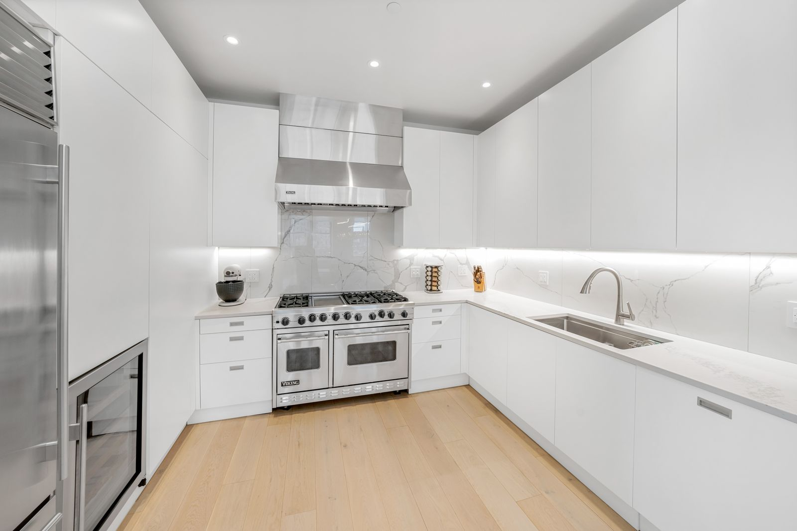 The renovated kitchen has white marble countertops running beneath flat-panel cabinetry with a six-burner Viking range centered along the back wall.