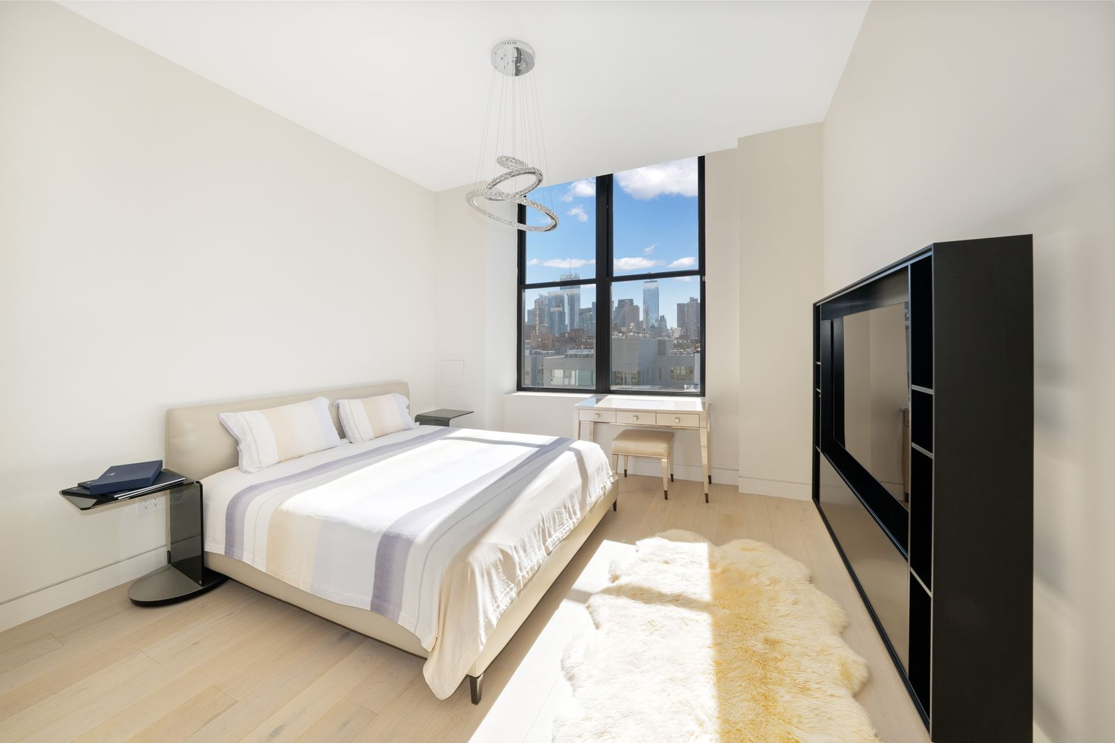The first suite places the bed beneath a silver ring chandelier, with a tall city-facing window pulling in natural light from the back wall.