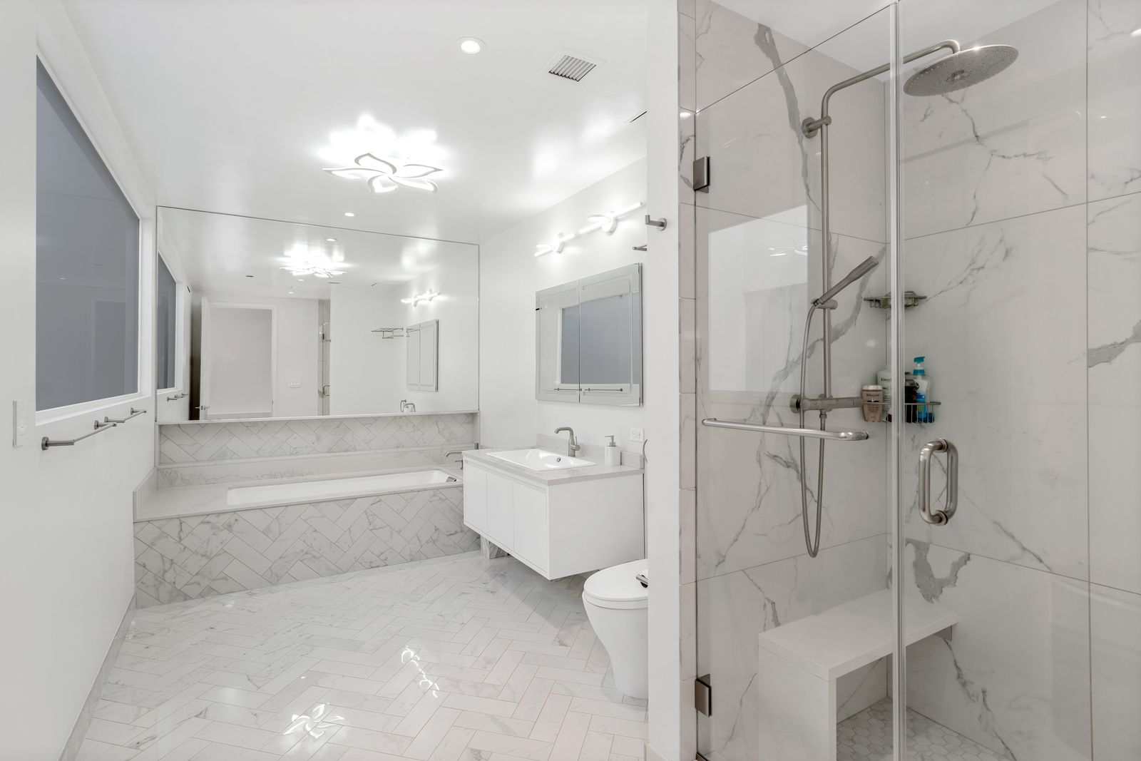 Marble bathroom with a deep soaking tub along the back, a floating vanity in front of it, and a glass-enclosed shower near the front of the room.