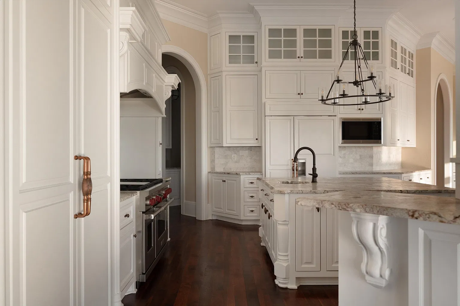 White cabinetry wraps around the kitchen and a center island sits beneath a wrought-iron chandelier.