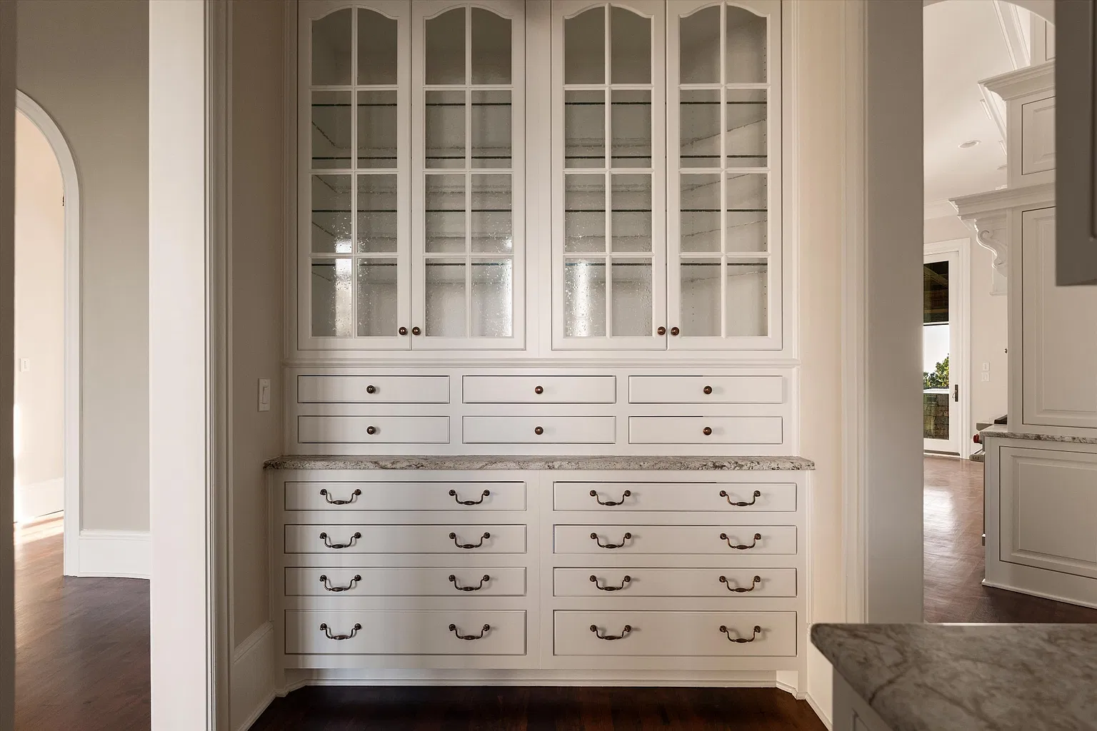 Butler's pantry with glass-front cabinetry rising above rows of drawers and a stone counter.