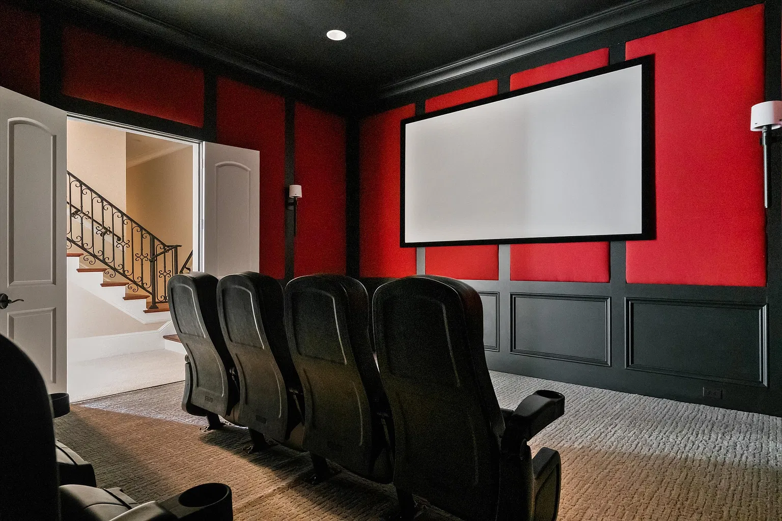 The walls are lined in black paint and red panels, with a large projection screen sitting across from rows of theater-style seating.