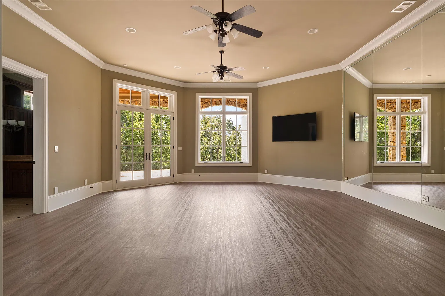 A spacious fitness center with mirrored walls and French doors opening to the outdoors. 
