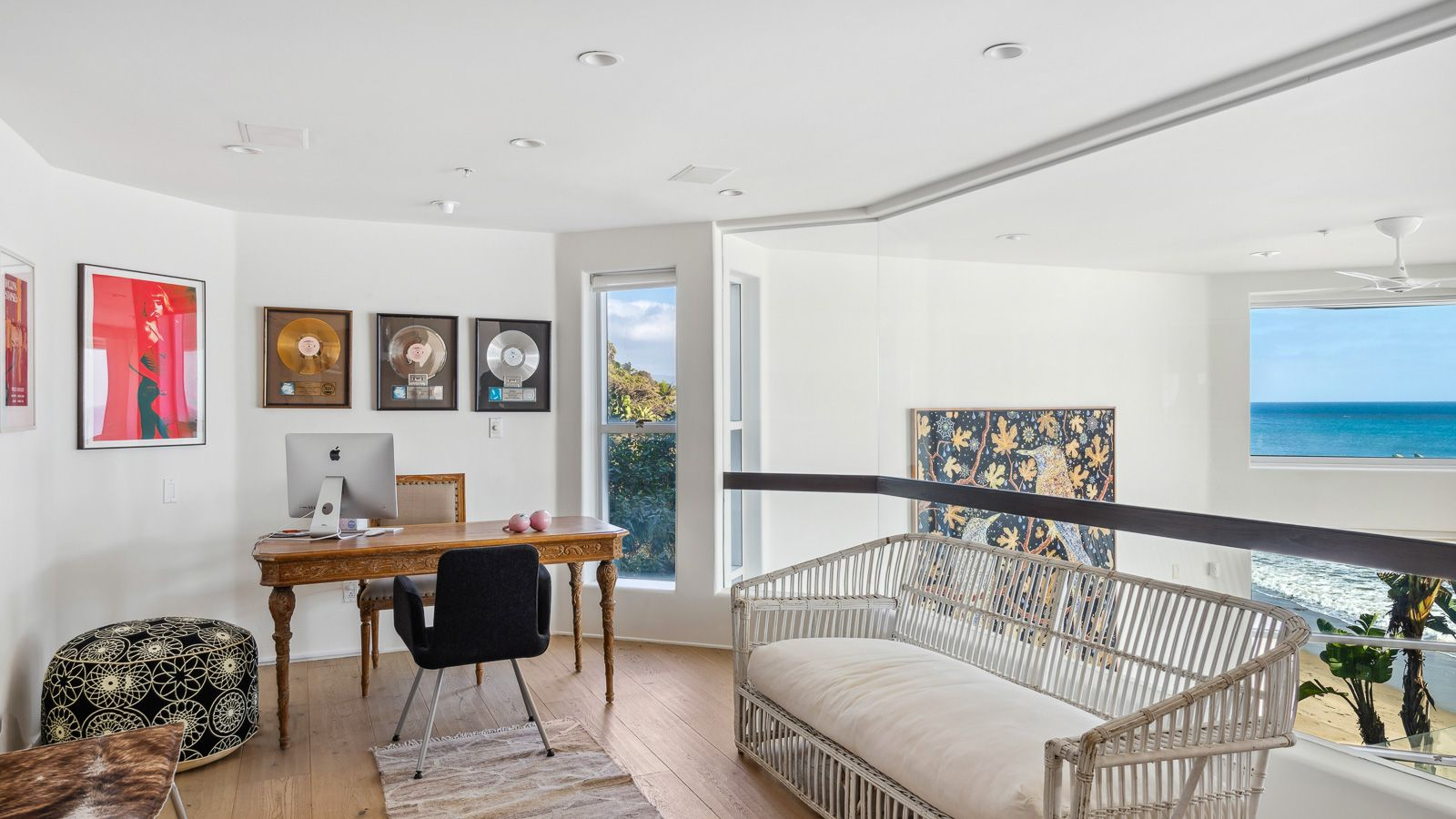 An office sits above the main living spaces, with a full wall of glass opening to sweeping ocean views. 