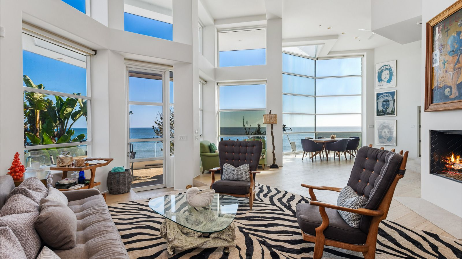 The main living area rises beneath soaring ceilings, with a wall of oversized windows continuing from the dining area.
