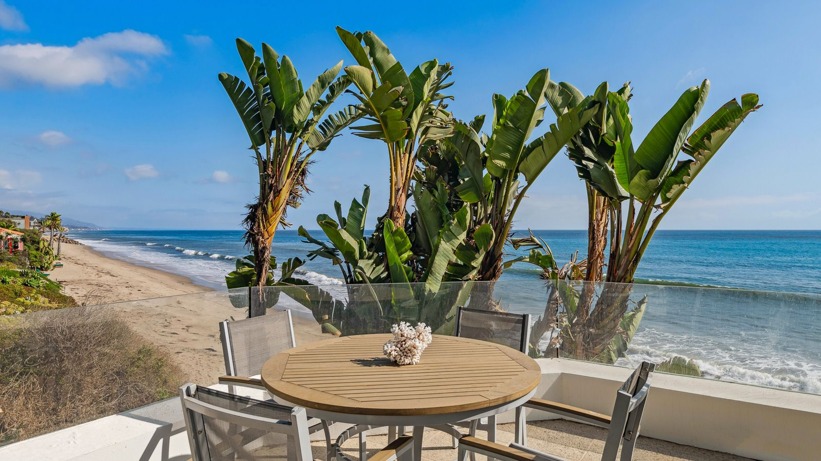 An outdoor dining terrace where a round table sits behind a glass railing.