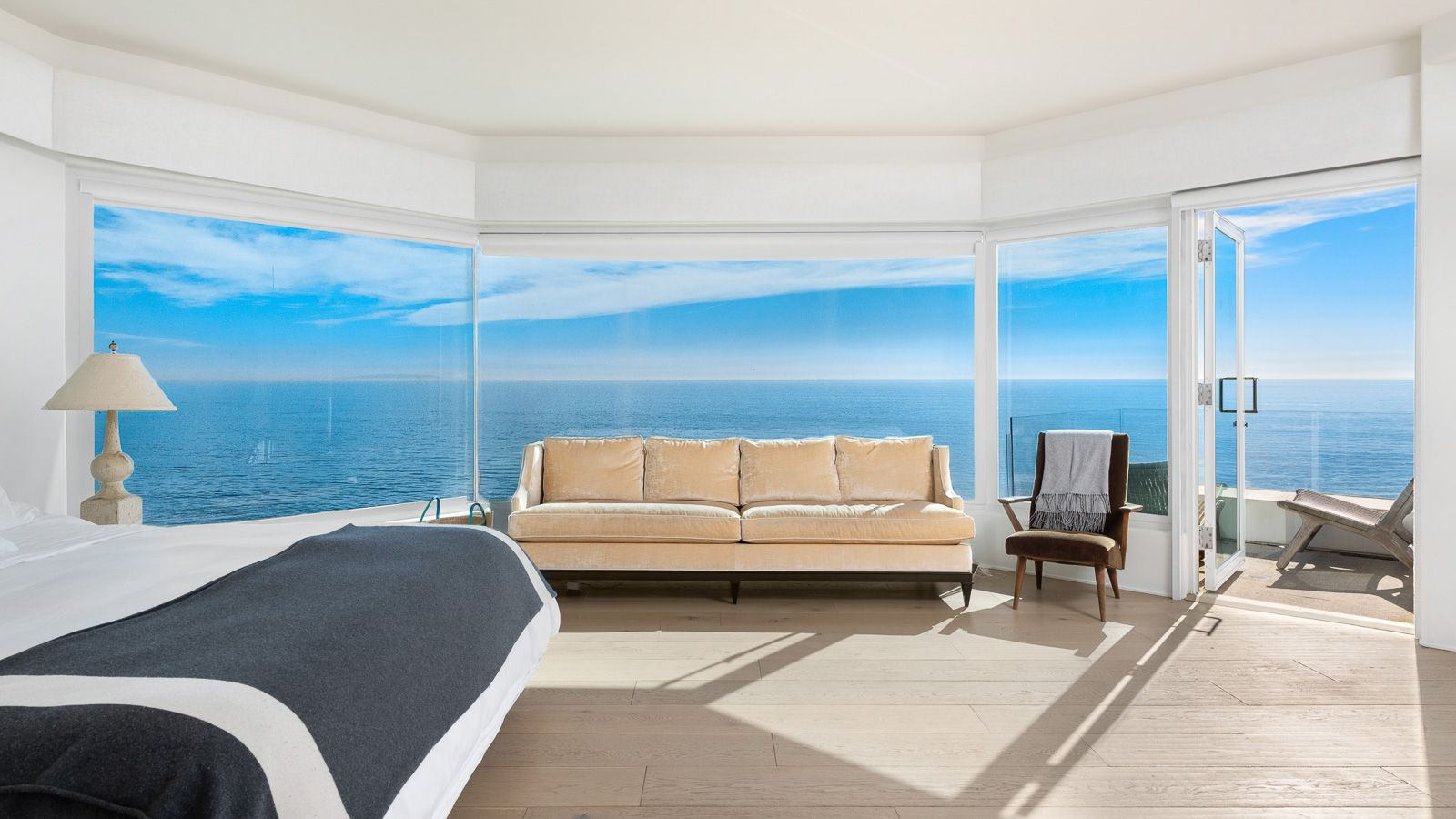The bed is positioned in front of a wall of windows that opens the room to one of the home’s best ocean views, with a door beside the glass leading to a small private balcony.