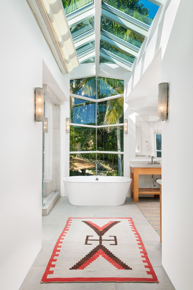 A freestanding soaking tub sits beneath the glass roof in the middle of the room,