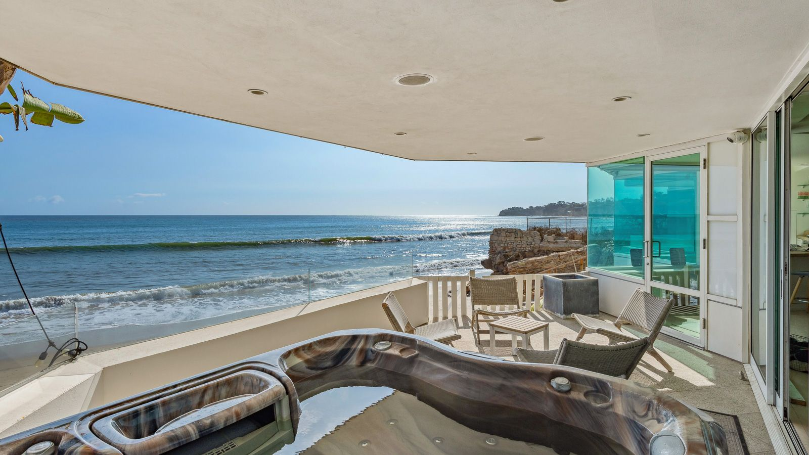 Stepping out on the terrace, a spa sits in the corner, and a small group of lounge chairs is gathered just before the beach entrance.