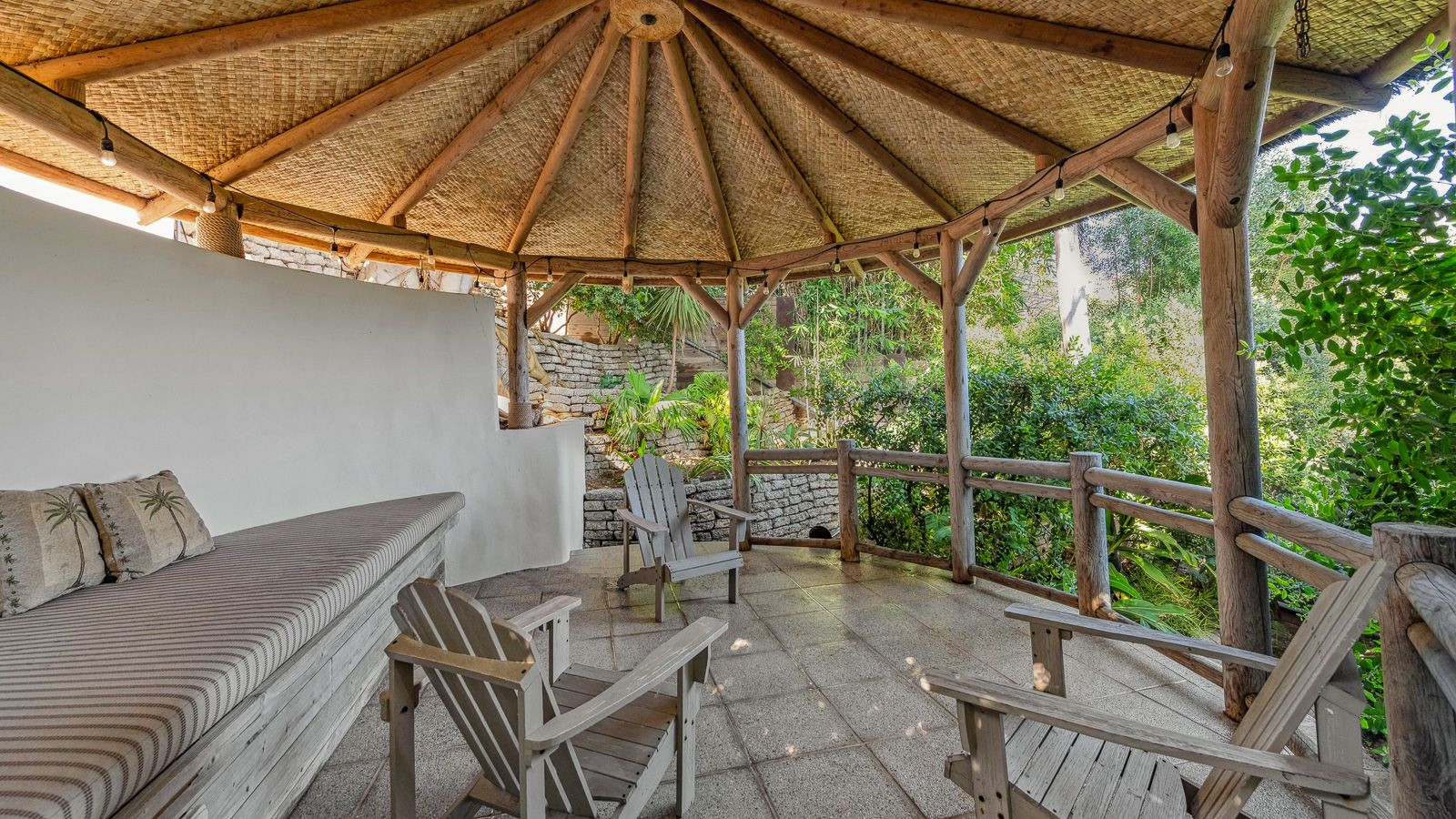 A covered pavilion sits beneath a woven roof with built-in seating and Adirondack chairs.