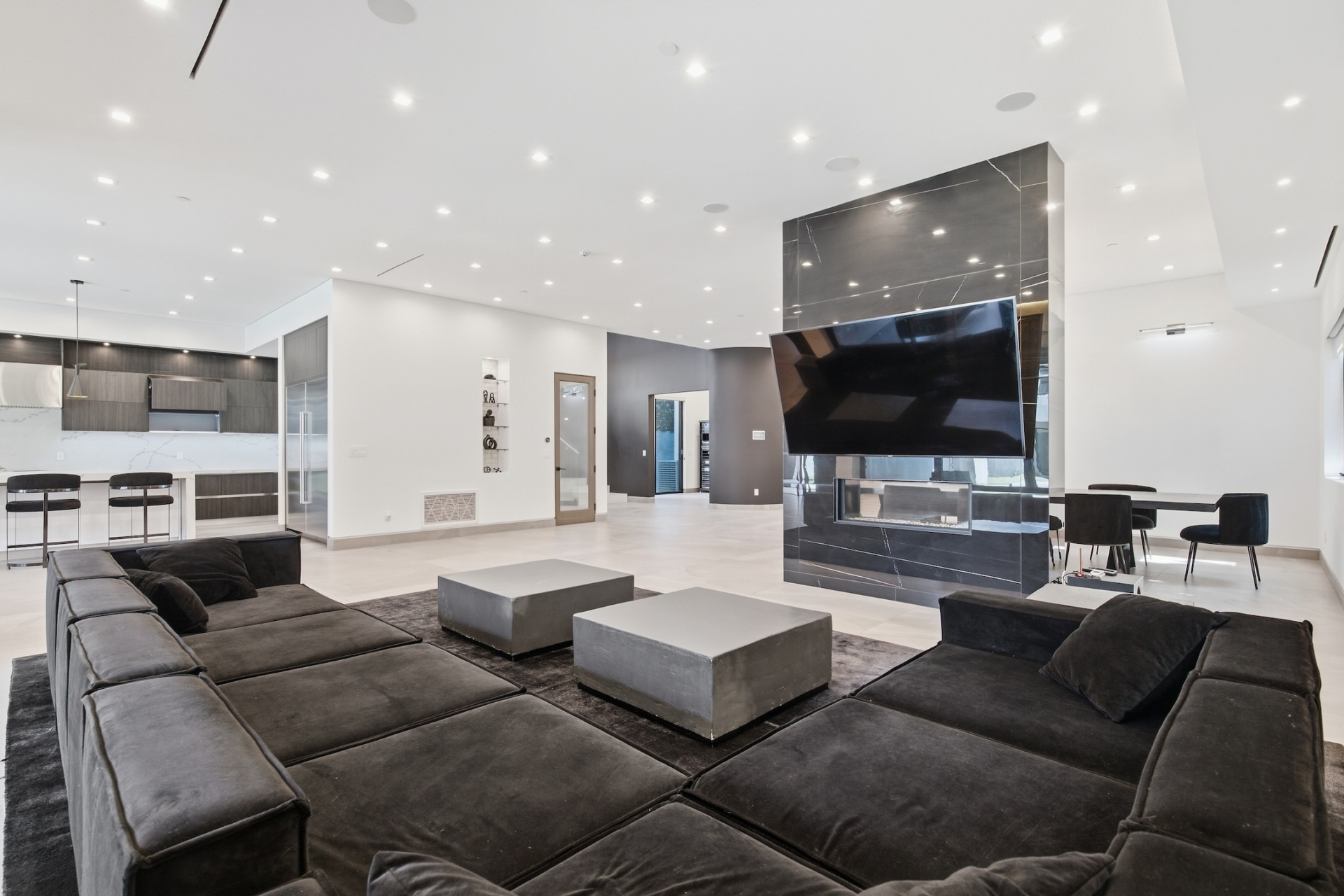 The living room sits at the back of the open main level, with a dark stone fireplace and mounted television forming one side of the space. 