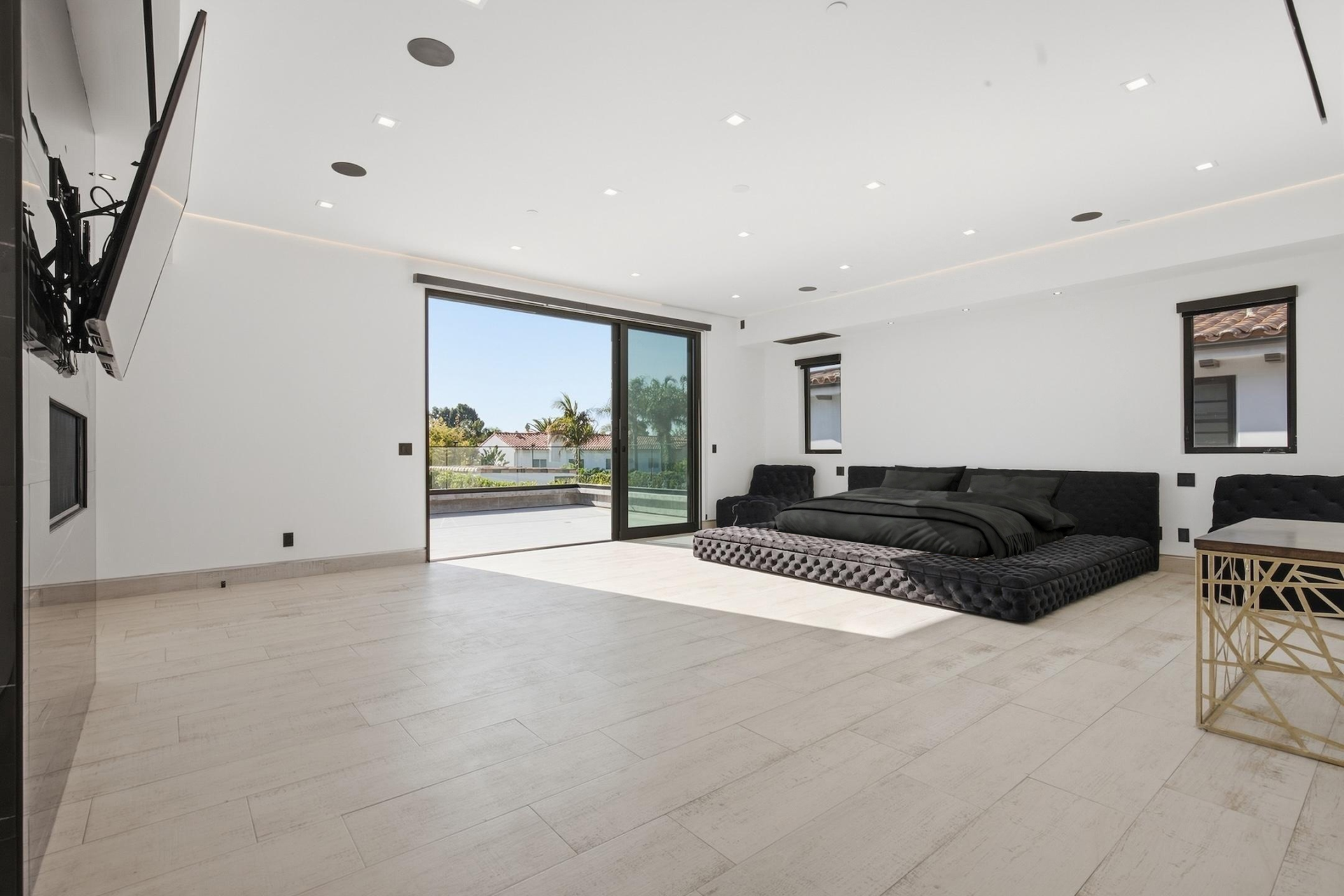 An oversized bedroom where the bed faces a dark stone fireplace and TV wall similar to the one downstairs in the living room. 