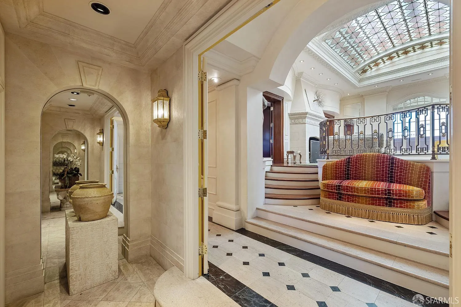 A marble-lined foyer is framed by arched mirrored panels and layered moldings before opening toward a short set of steps.