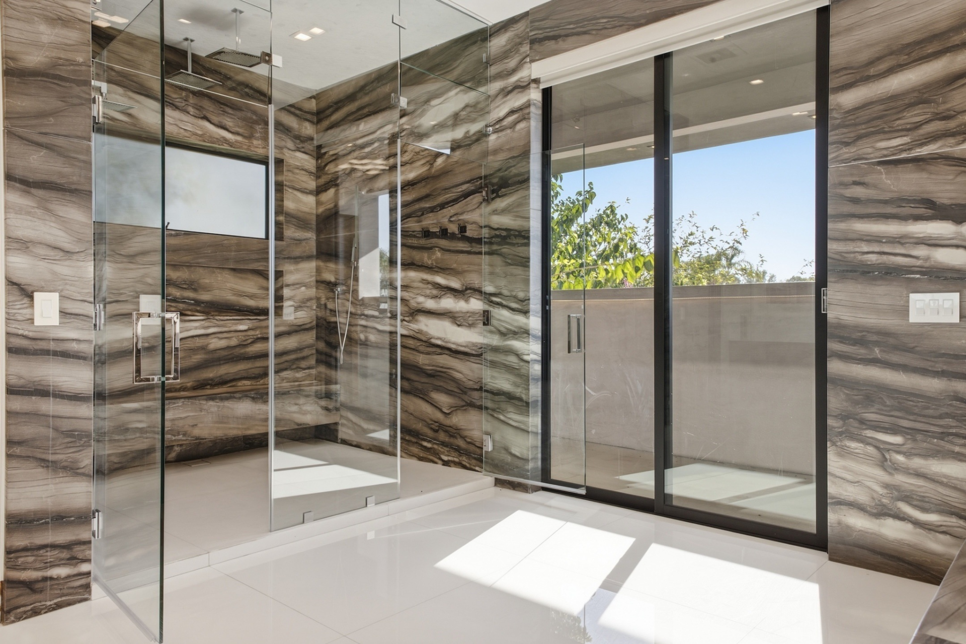 The stone continues across the walls to a large glass-enclosed walk-in shower.